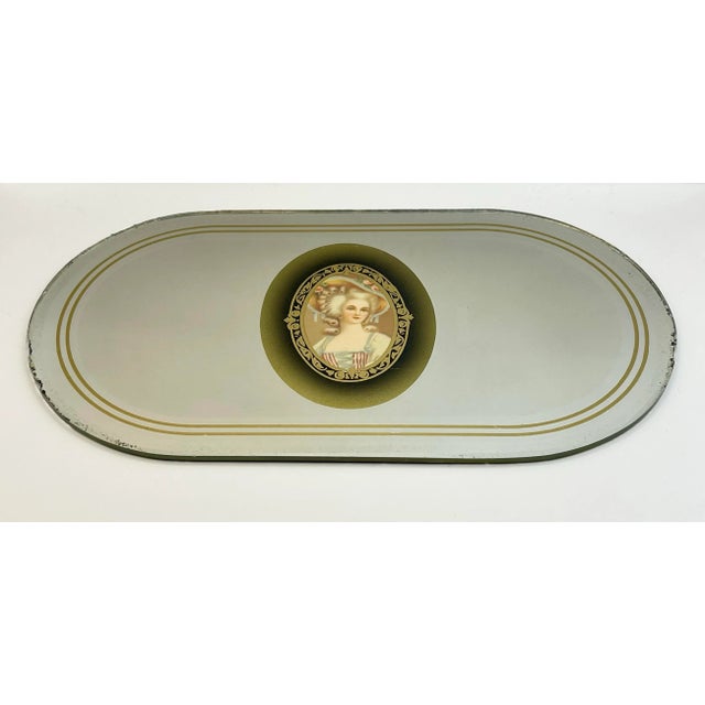 A vintage tabletop vanity mirror with a portrait of Marie Antionette in the center and banded at the edge with two gold...