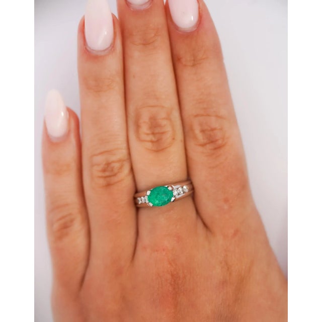 1.17 carat oval cut emerald ring, half bezel east west set with all natural mined gemstones. Adorned with 6 round cut...