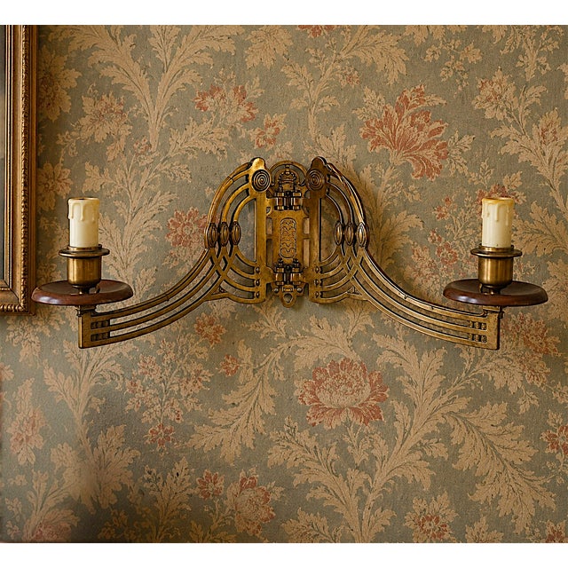 A striking vintage double wall sconce in aged brass, designed around a dramatic symmetrical composition. Two candle-style...