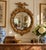 A Federal-style giltwood convex mirror crowned with a carved eagle, its wings outstretched above a laurel motif—an...
