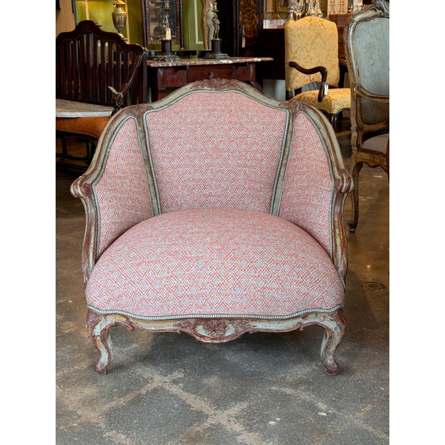 A painted Italian bergère with a shaped back, scrolled arms, carved floral cresting, and a serpentine apron on cabriole...