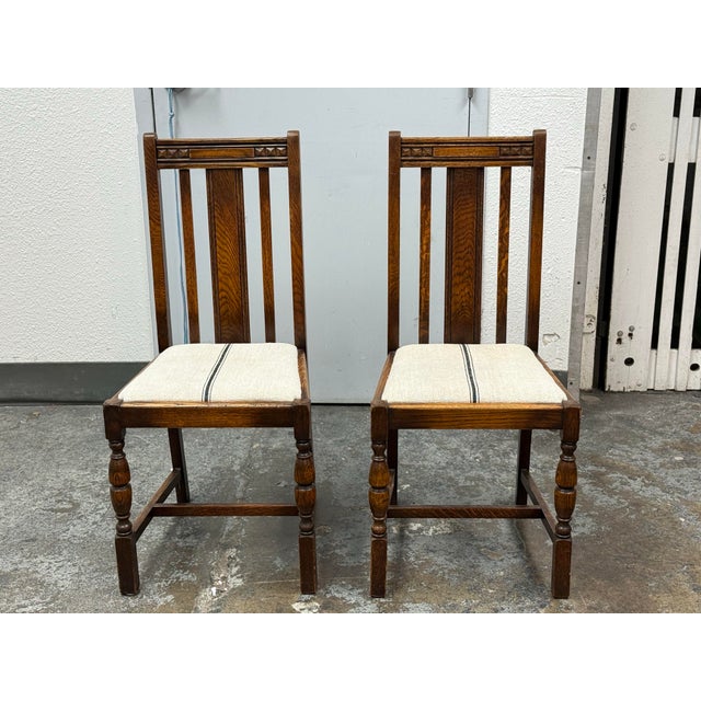 Design Plus Gallery presents a Pair of Antique Jacobean Revival Oak Upholstered Side Chairs. Each chair has a tall slatted...