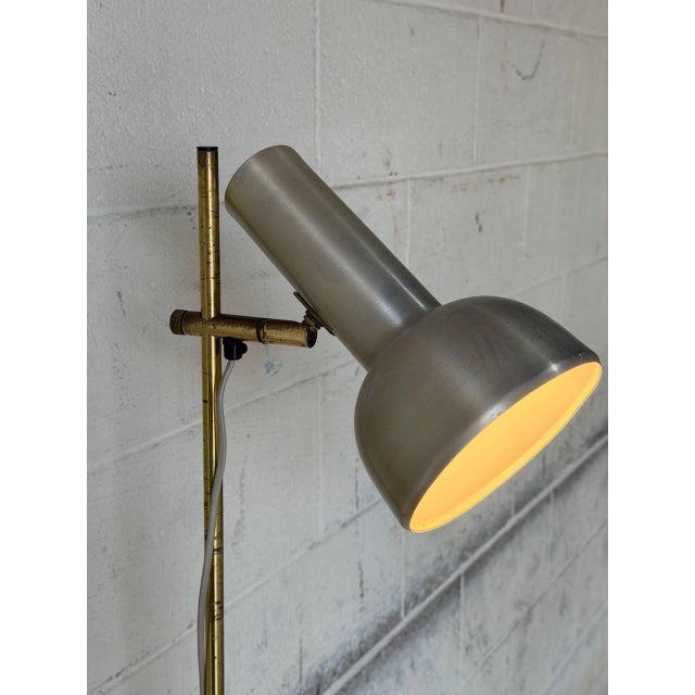 This sleek floor lamp features an adjustable spotlight shade mounted on a slender stem. The minimalist design offers...