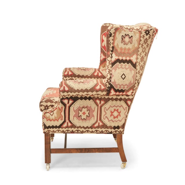 A 20th c. George III style wingback chair upholstered in an antique Kilim rug on casters. Wood frame is in good condition...