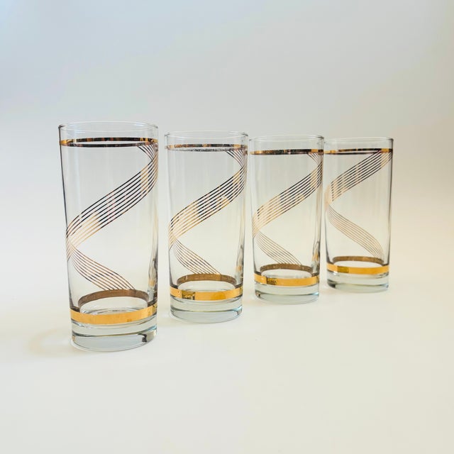 A set of 4 mid century highball tumblers. Each is decorated in metallic gold lines that spiral around the sides of the...