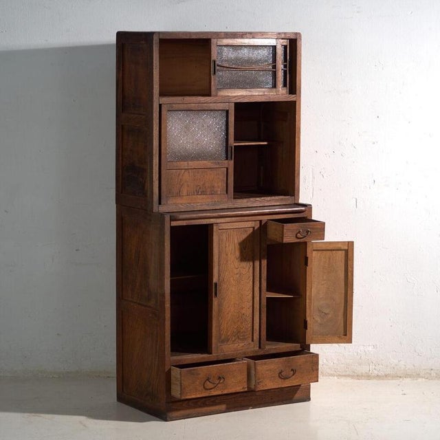 This antique Japanese mizuya dansu in keyaki wood is a two-part kitchen cabinet with sliding doors and textured glass. It...