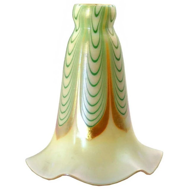 An antique Art Nouveau art glass, floriform lamp shade with a ruffled edge. It is decorated with green dragged loop with a...