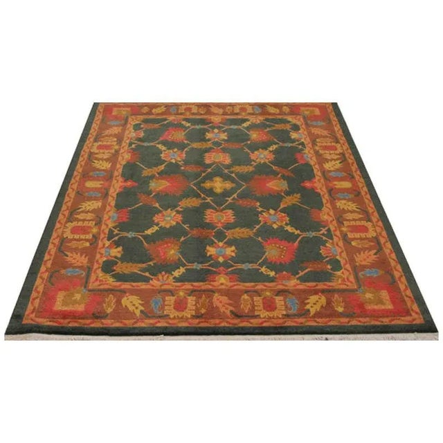 Handwoven Rug featuring a Tibetan design on a green colored field and rust border, accented in shades of light blue, red,...