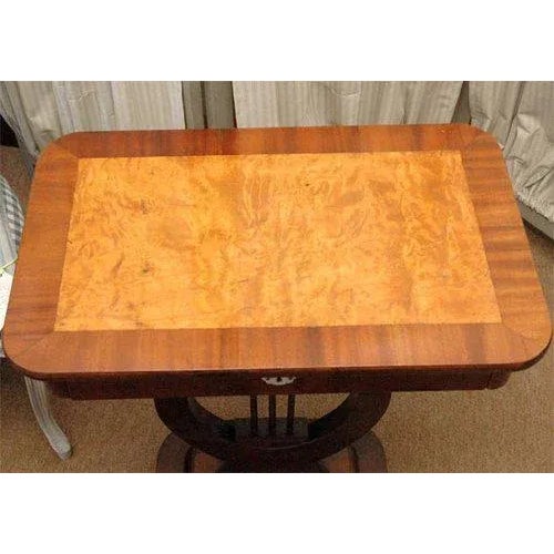 This table has a central support in the shape of a lyre which supports a single drawer having a brass lock and mother of...