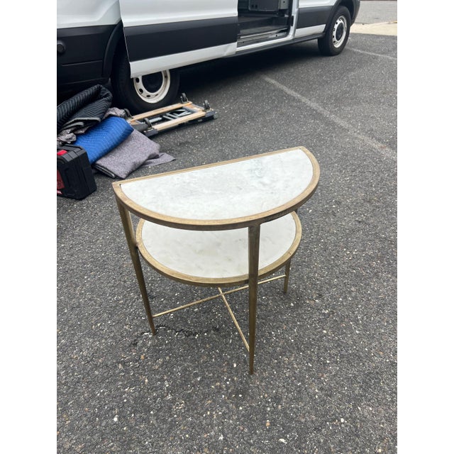 A refined two-tier accent table featuring elegant white marble surfaces framed in warm brass-toned metal. The unique...