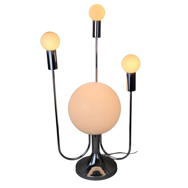 A sculptural Space Age table lamp from the 1970s orbit-lamp family: a polished chrome trumpet base rises to a large...