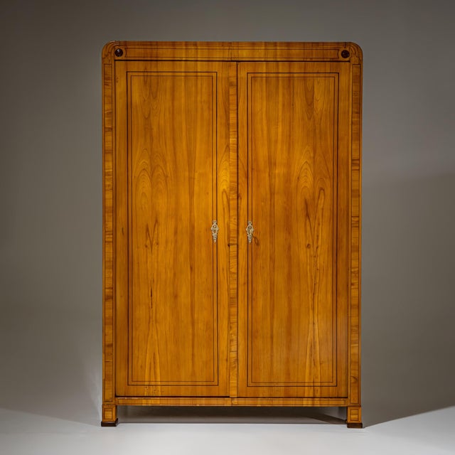 Elegant two-door Biedermeier wardrobe in cherry veneer, featuring rounded upper corners and square plinth legs. The front...