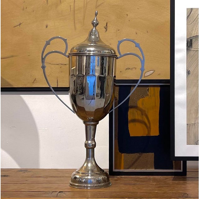 A striking vintage silver plate trophy urn with elegant twin handles and a lidded finial top, raised on a pedestal base....