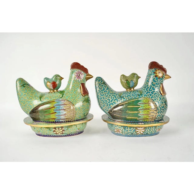These are two very detailed cloisonne boxes in the form of nesting chickens. The principal color of one box is a pale...