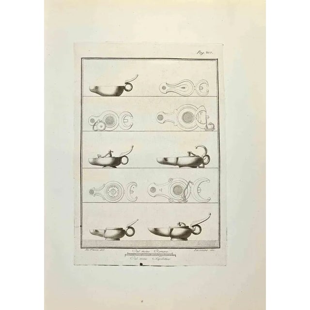Oil Lamp from "Antiquities of Herculaneum" is an etching on paper realized by Iacomino e Nicola Vanni in the 18th Century....