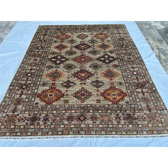 This beautiful hand-knotted wool area rug features a classic Afghan Kazak tribal style. The center field has a warm grey...