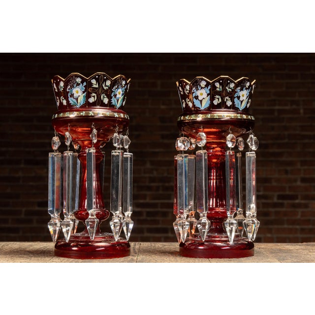 A striking pair of ruby red glass mantle lusters, each featuring hand-painted enamel floral decoration with gold...