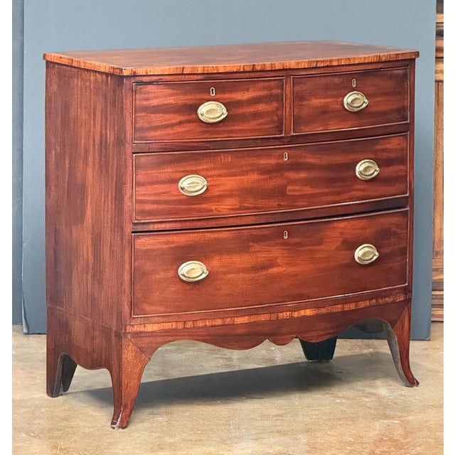 A handsome English bow-front chest of drawers of mahogany in the Georgian style, featuring a bowed top with a beautiful...