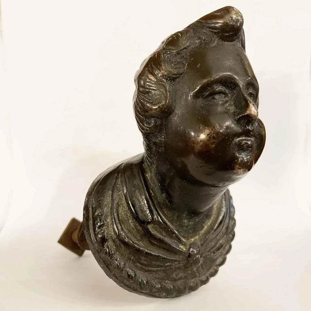 Bronze bust from the 17th century depicting a young boy with wavy hair and a robe gathered at the neck, ending in an oval...
