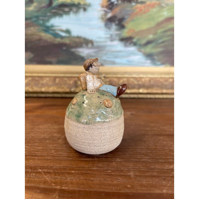 Charming handmade studio pottery incense holder featuring a whimsical seated figure perched atop a rounded base. The...