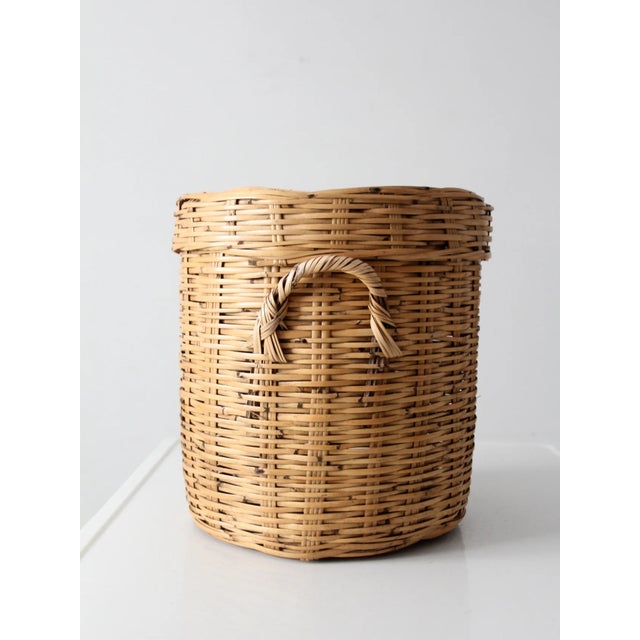 A lidded wicker basket with a rounded silhouette and softly flared rim, woven in a tight, even pattern with a warm natural...