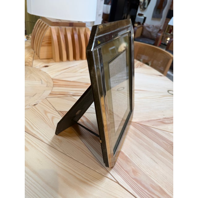 A vintage picture frame with a deep, angular profile, polished metal edges, and a warm brass-tone surround. Its layered...