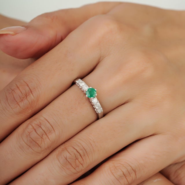 This contemporary 925 sterling silver ring features a vibrant 0.32-carat natural round emerald at the center, secured in a...