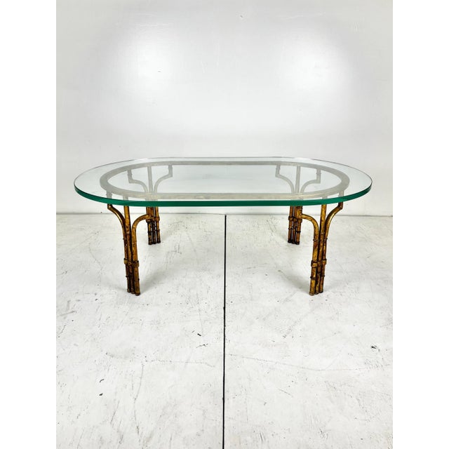 Vintage gilt gold faux bamboo coffee table with oval glass top. The metal frame has a beautifully aged mottled gilt...