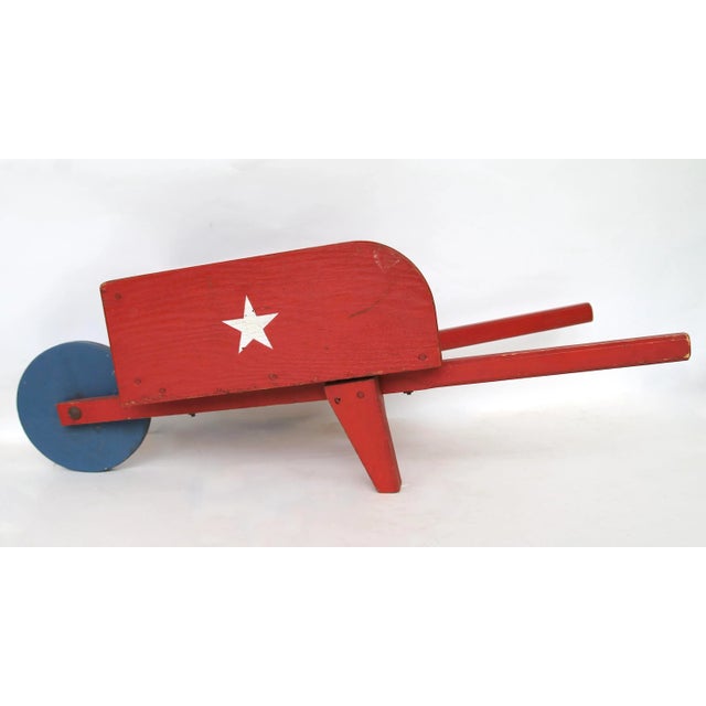 Circa 1940s handmade and painted wood child's wheelbarrow in red, white and blue with star on each side. Wheelbarrow is...