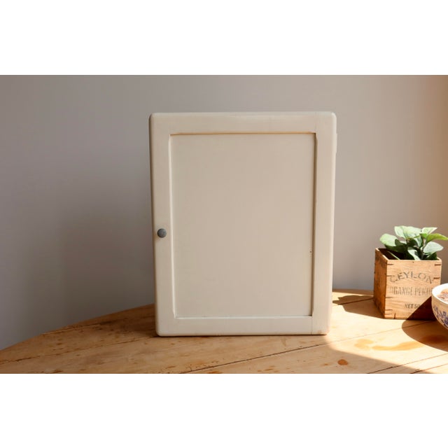Ivory-painted wooden wall-mounted medicine cabinet with a simple and functional design. The interior features two glass...