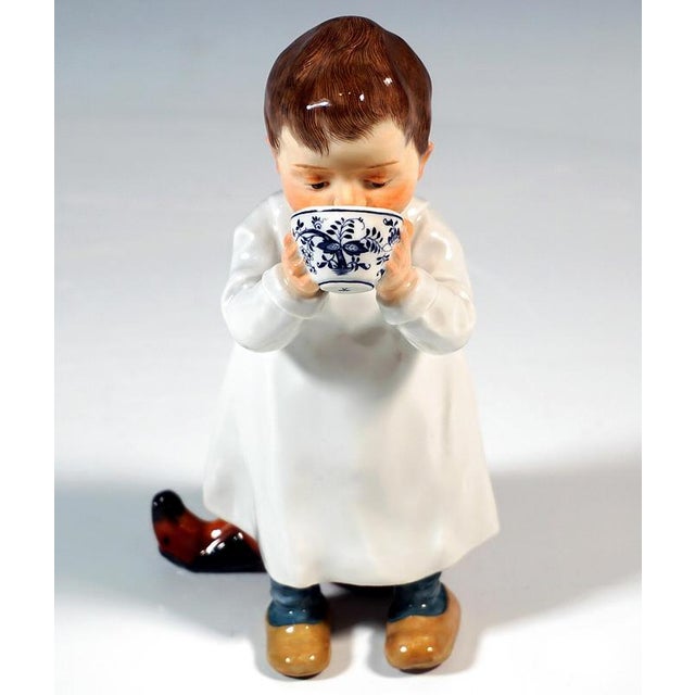 Boy in a nightgown standing in front of a damaged wooden horse, holding an onion pattern cup with both hands and drinking...