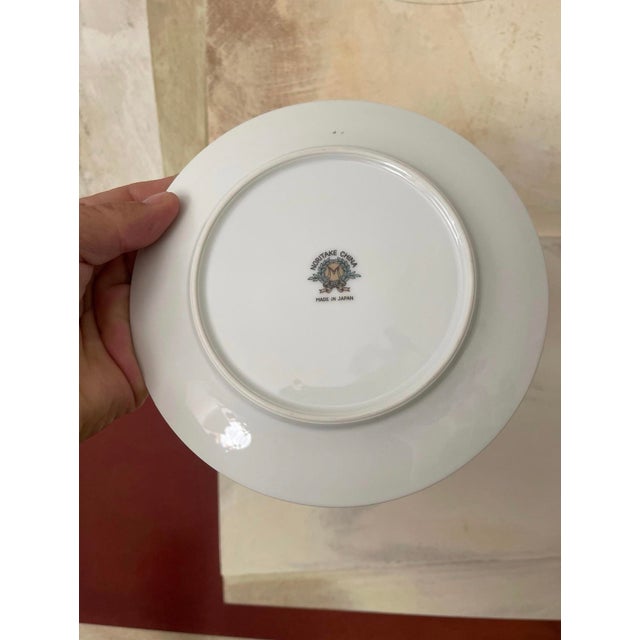 Lovely set of 9 vintage 6.5” plates, made in Japan by Noritake. Presented on a crisp white with a gold rim, a geranium...