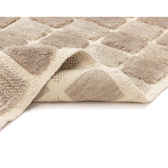 A soft grid of tonal squares unfolds across ivory and misty taupe, giving this rug the quiet rhythm of a checkerboard...