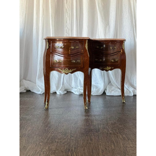 This elegant pair of French Louis XV-style nightstands features beautifully shaped bombe fronts, cabriole legs, and warm...