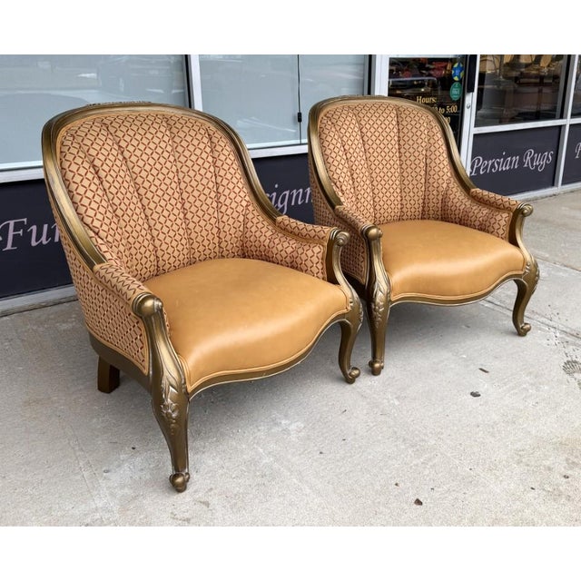 This pair of upholstered bergère chairs features gracefully carved frames with a warm gilt-toned finish, elegant cabriole...