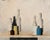 This artwork presents a serene still life composition featuring a collection of bottles and jars in a muted palette. The...