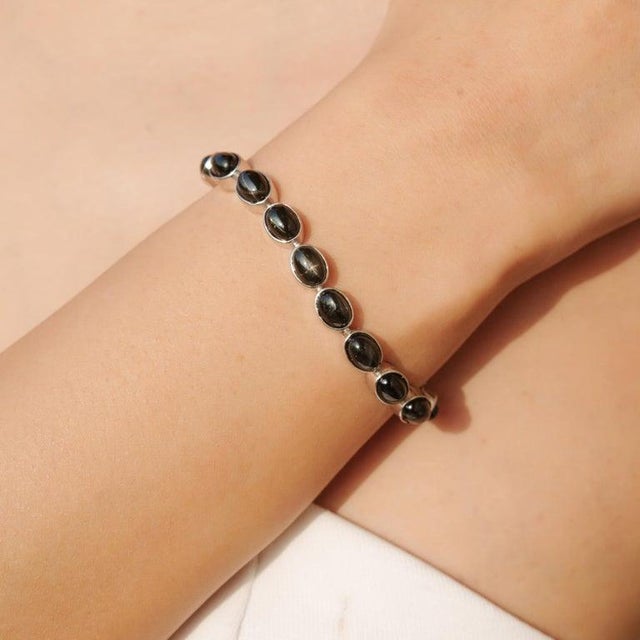 Crafted in 925 sterling silver, this elegant tennis bracelet features 21 natural black star gemstones in a smooth oval...