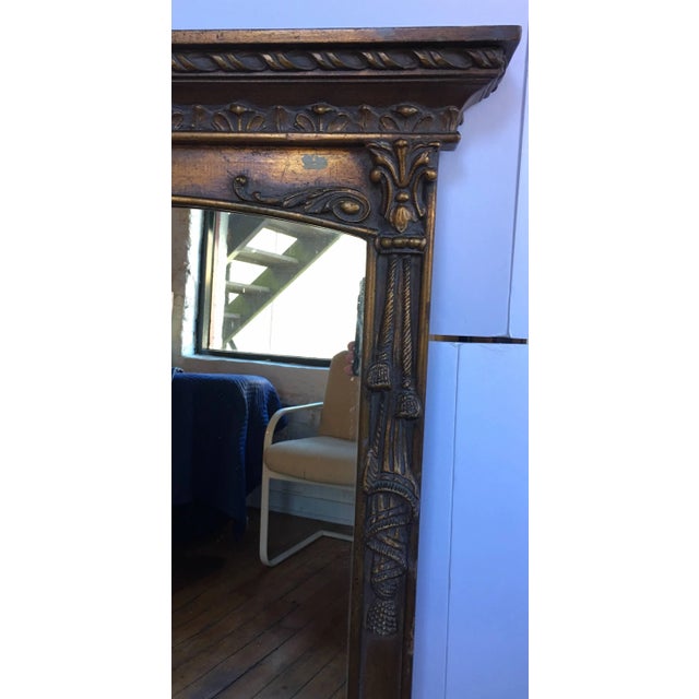 Tall Regency style carved wood wall mirror featuring draped tassel form detailing and original gold painted finish.