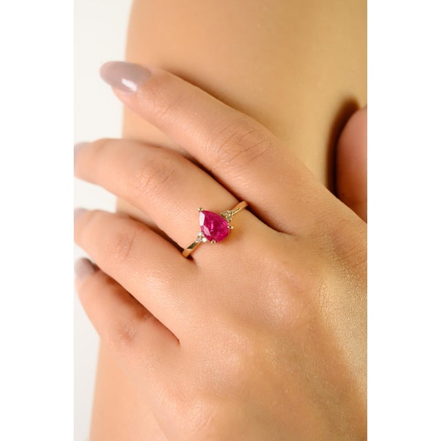 This elegant engagement ring showcases a captivating pear-cut natural ruby weighing 1.21 carats, set in lustrous 14K...