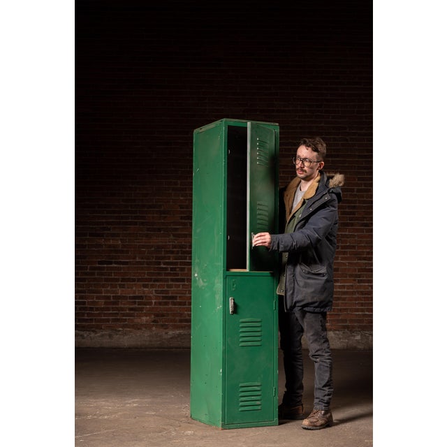 Tall two-tier steel locker cabinet in original green paint, featuring vented doors and simple latch hardware. The unit is...