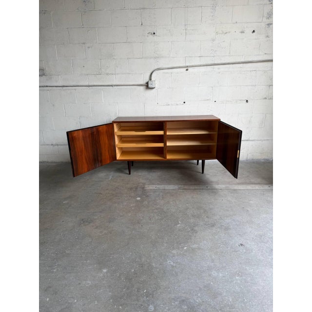 This exceptional low-profile sideboard credenza features a streamlined architectural form standing on elegant dark tapered...