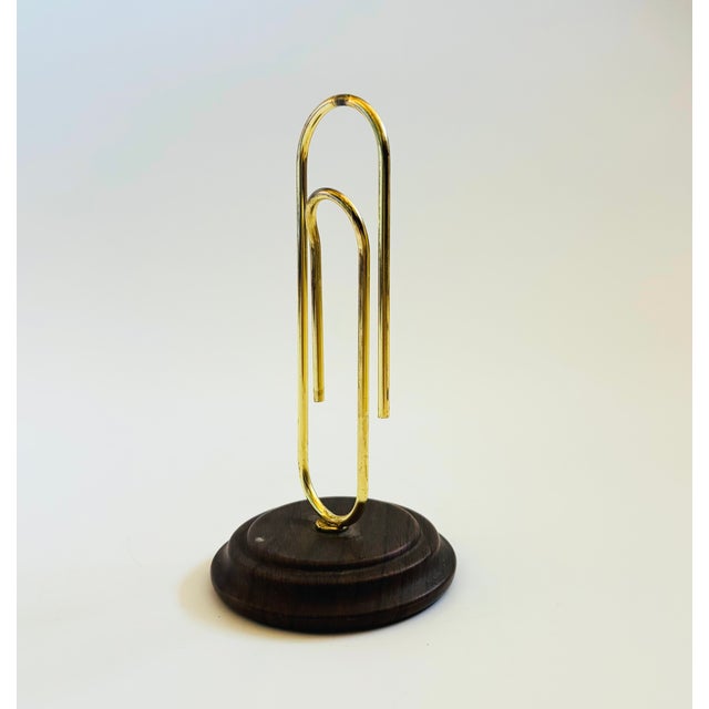 A vintage oversized brass paperclip for holding letters, notes, or displaying photos on a circular wood base.