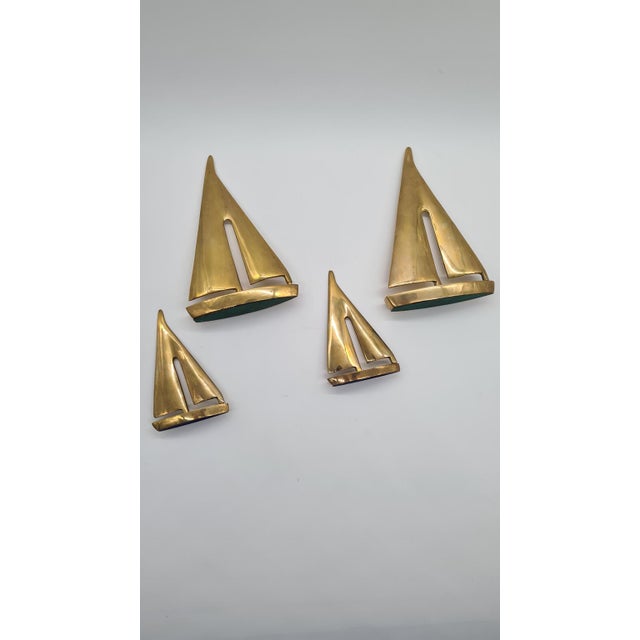 A set of four sailboat figurines from the 1970s, made of solid brass in a warm golden hue. Each figurine has a minimalist,...