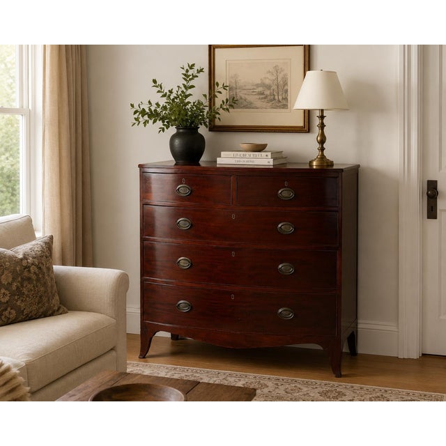 A handsome 19th-century English bowfront chest of drawers, masterfully crafted from richly figured mahogany. Featuring an...