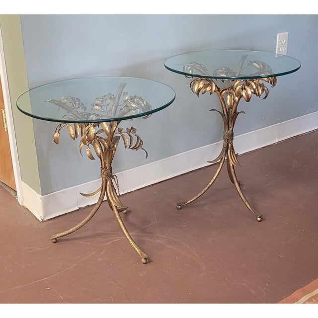 A pair of fine guilt metal Italian Hollywood Regency end tables with glass tops. Each features branches of Palm leaves in...