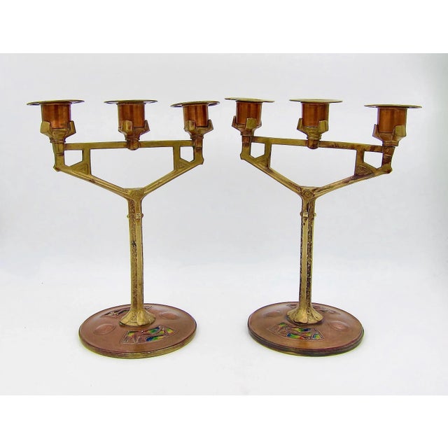 An antique pair of three-light candle holders in copper and brass with multi-colored enamel accents, crafted at the...