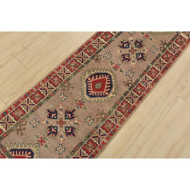 A tribal Caucasian Kazak runner hand-knotted with fine wool on a cotton foundation. This rug features geometric medallions...