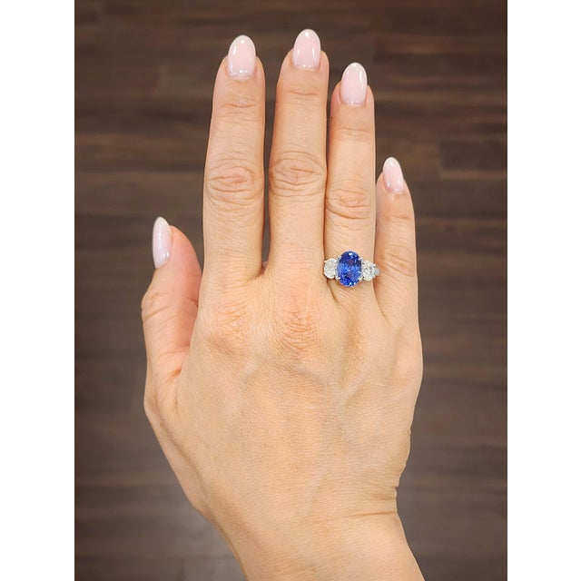 A captivating 4.25-carat oval-cut sapphire commands attention with its deep blue hue. Accentuated by two 1.00-carat oval-...