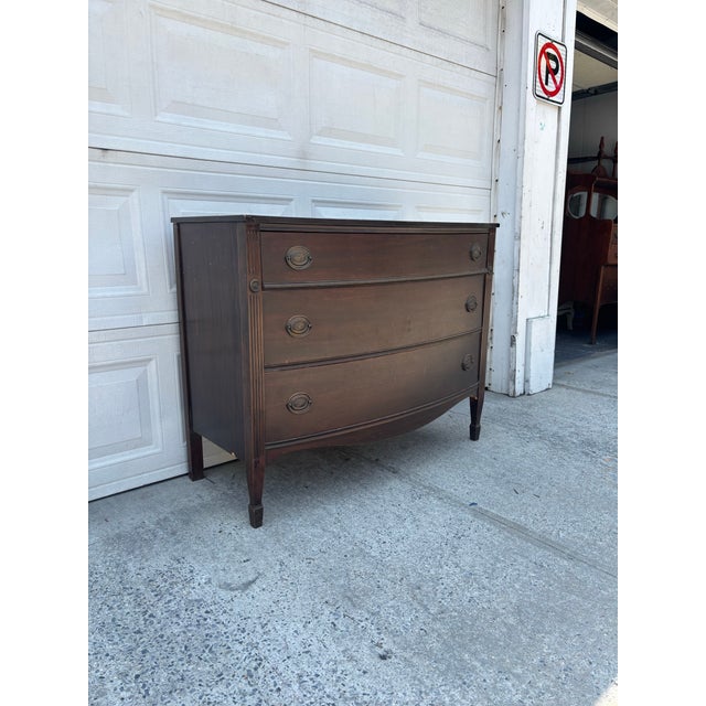 We have a beautiful vintage Federal Revival bowfront dresser for sale. It features a classic Hepplewhite silhouette,...