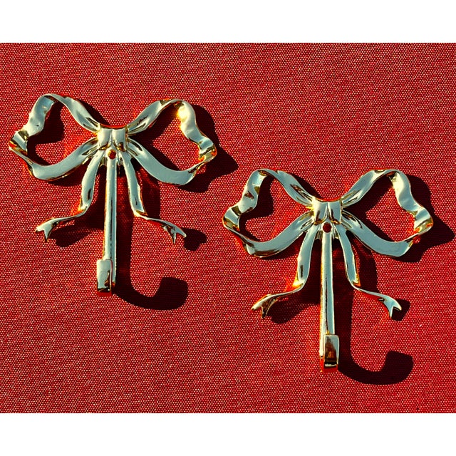 Pair of brass bow wall hooks. Each bow is crafted to resemble a ribbon tied into a classic bow shape, with loops on both...